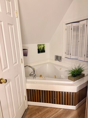 Un baño moderno con una bañera independiente, un panel de madera decorativo, un lavamanos pequeño empotrado en la pared y una ventana con contraventanas blancas.