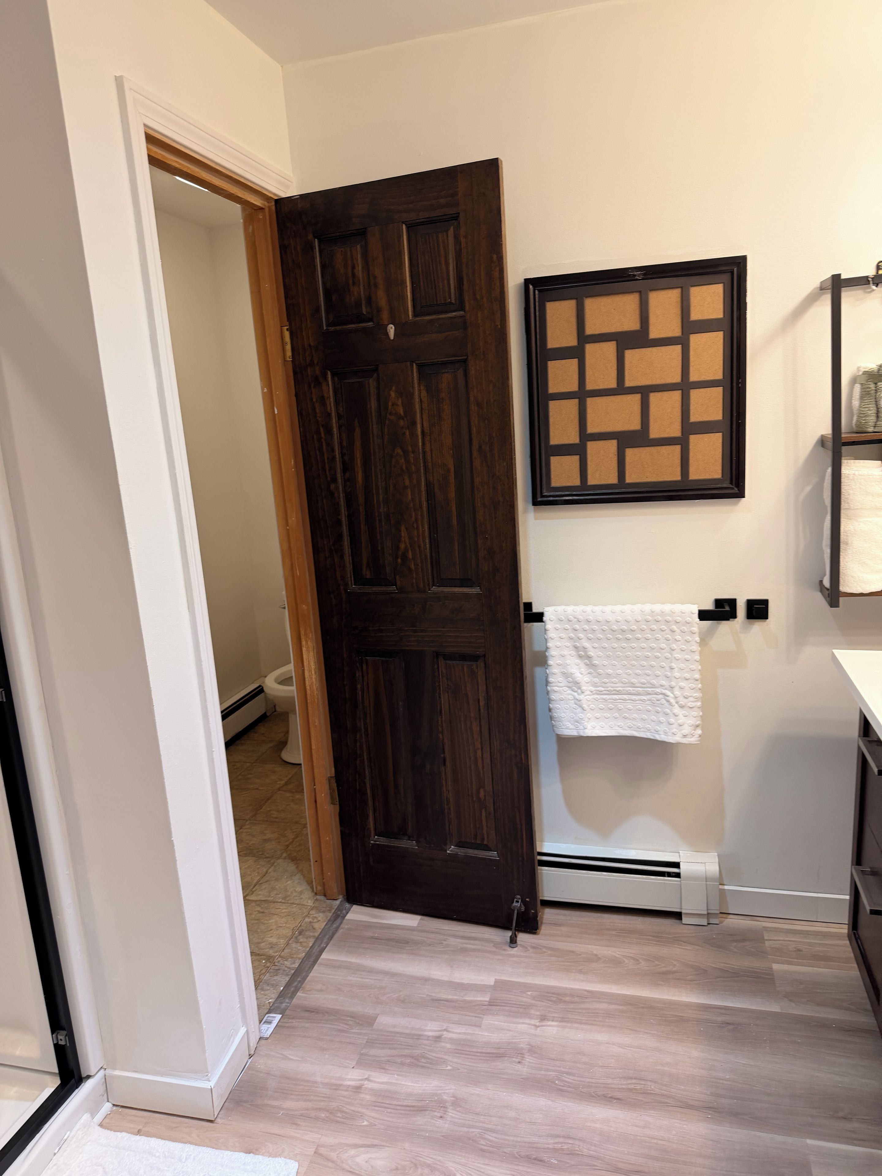 Een badkamer met een houten deur, een handdoekrek, een handdoek en een wandgemonteerde handdoekwarmer.