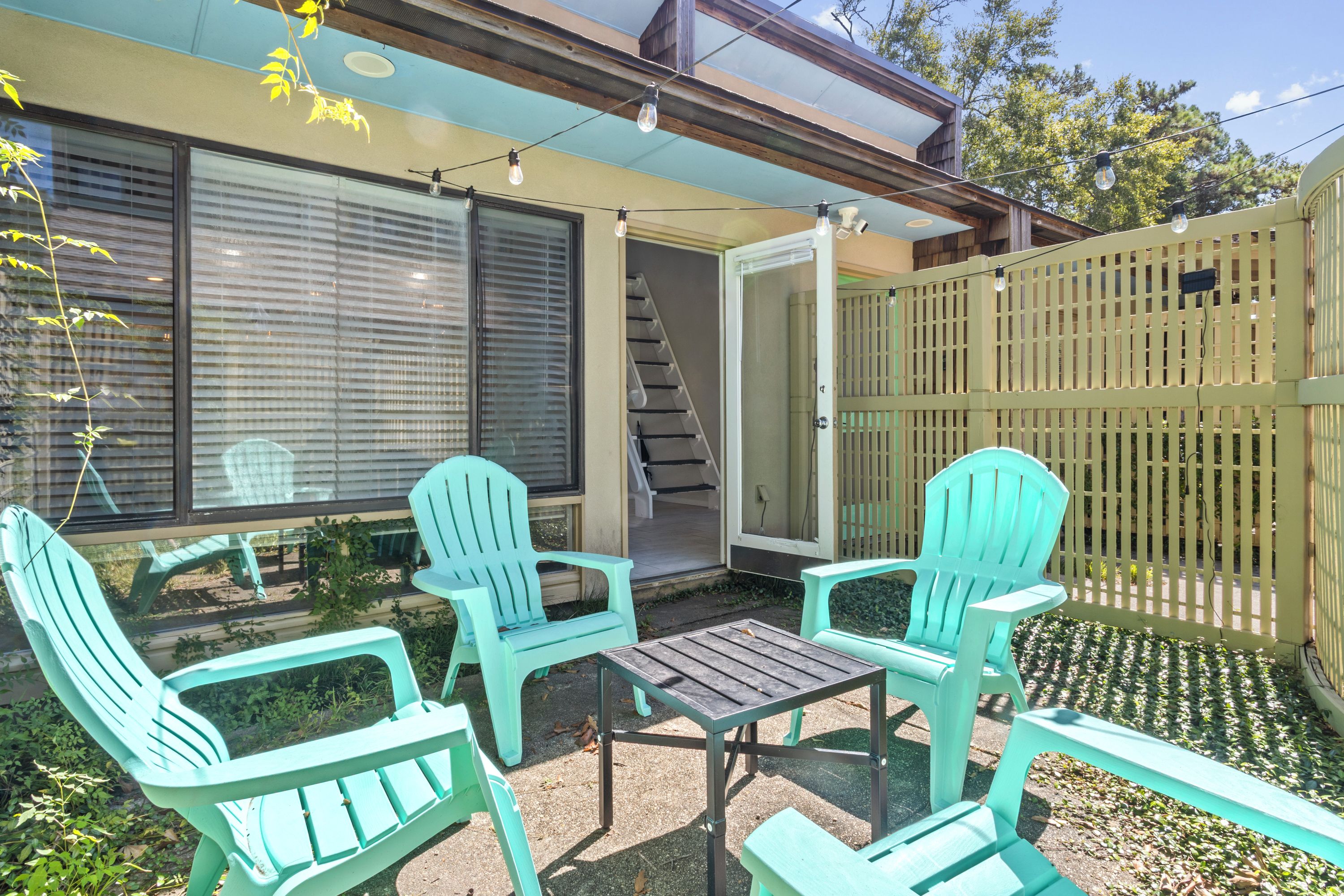 Un espace patio avec deux chaises turquoise et une petite table, une clôture en bois et un escalier menant à un niveau supérieur.