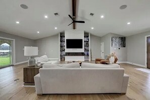 Un salón amplio con un sofá blanco grande, un televisor de pantalla plana montado en la pared y un ventilador de techo.