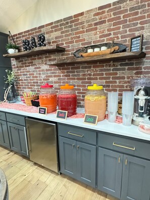 Zona de bar con pared de ladrillo, estante con un letrero que dice 'BAR' y mostrador con dispensadores de bebidas etiquetados.