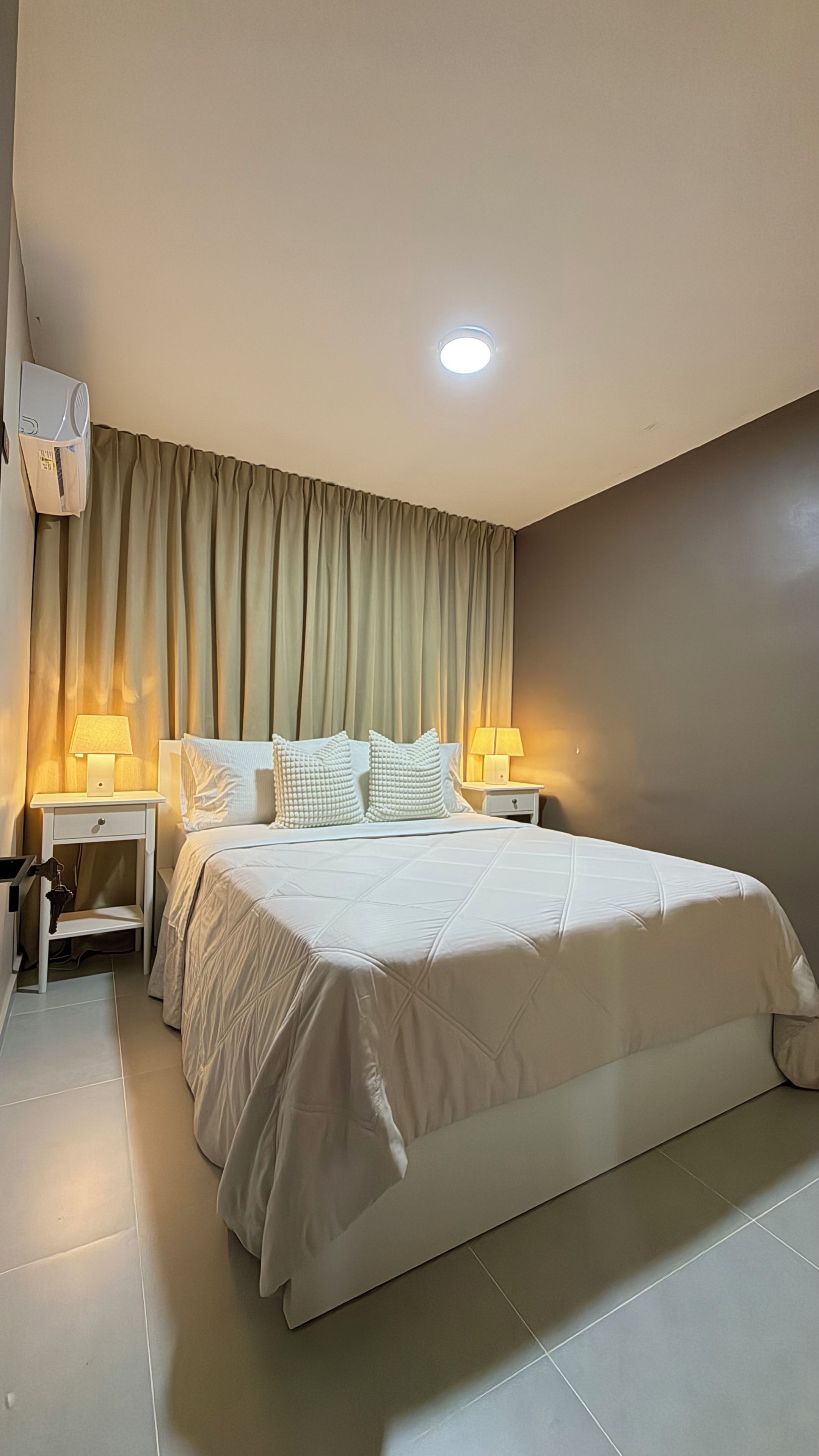 Une chambre d’hôtel avec un grand lit, deux tables de chevet avec des lampes, un luminaire au plafond et un climatiseur fixé au mur.