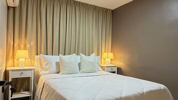 Une chambre d’hôtel avec un grand lit, deux tables de chevet avec des lampes, un luminaire au plafond et un climatiseur fixé au mur.