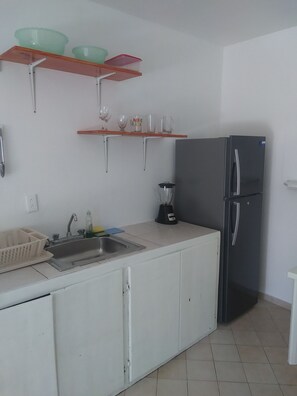 A kitchen with a sink, a refrigerator, and shelves with bowls and glasses. -  Encuentro Beach hidden gem / 1 Br, a/c, Internet, pool, backup electricity (Cabarete)