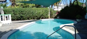 A swimming pool with a stone deck, surrounded by lush greenery and a white fence. -  Encuentro Beach hidden gem / 1 Br, a/c, Internet, pool, backup electricity (Cabarete)