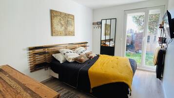 A bedroom with a bed, a wooden bedside table, a large window, and a view of the outdoors.