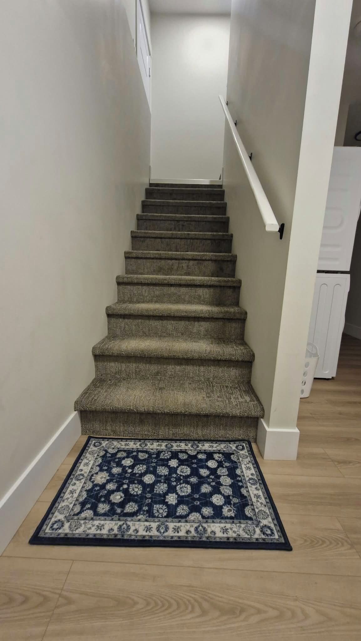 Un escalier recouvert de moquette, avec un tapis à motifs au bas.