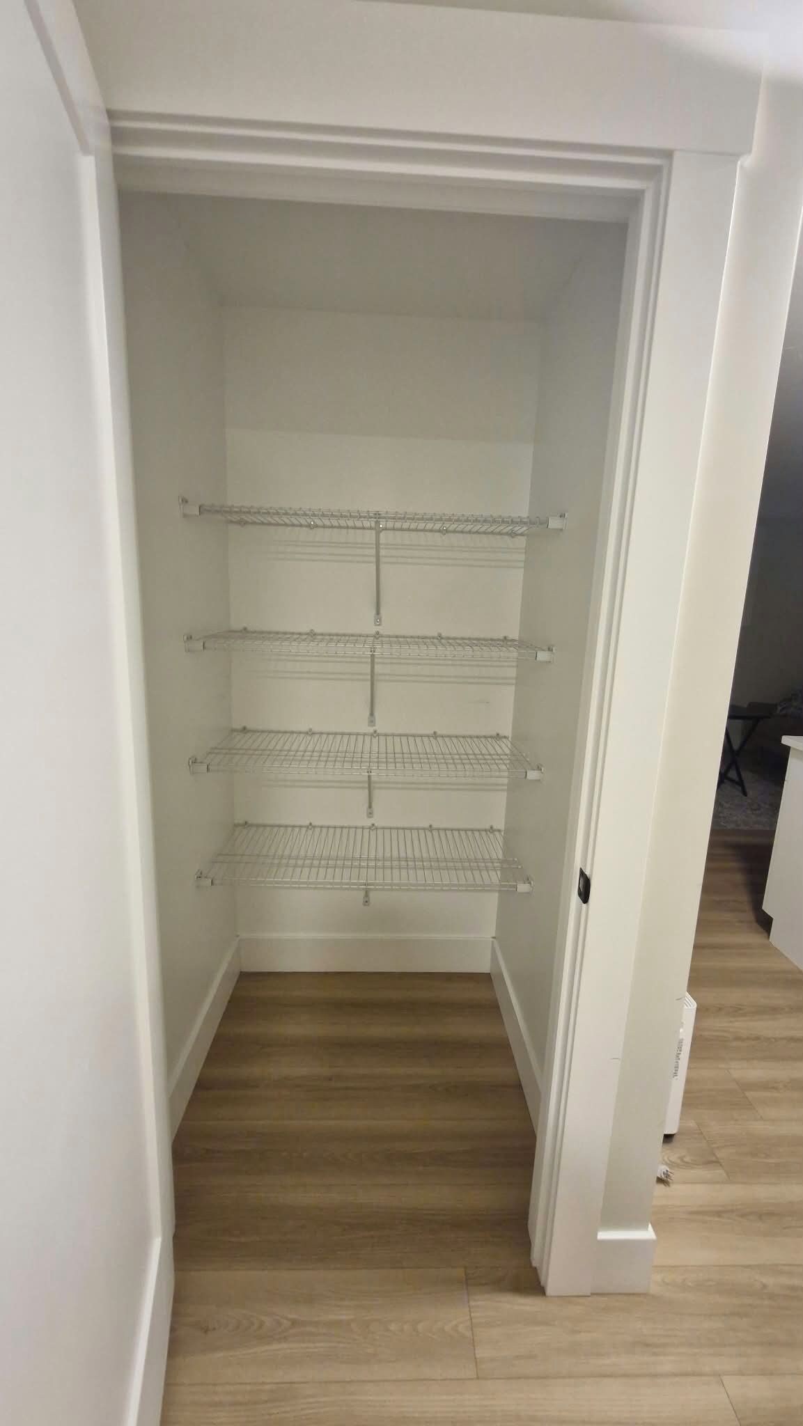 Un placard blanc avec trois étagères en fil de fer et un plancher en bois.