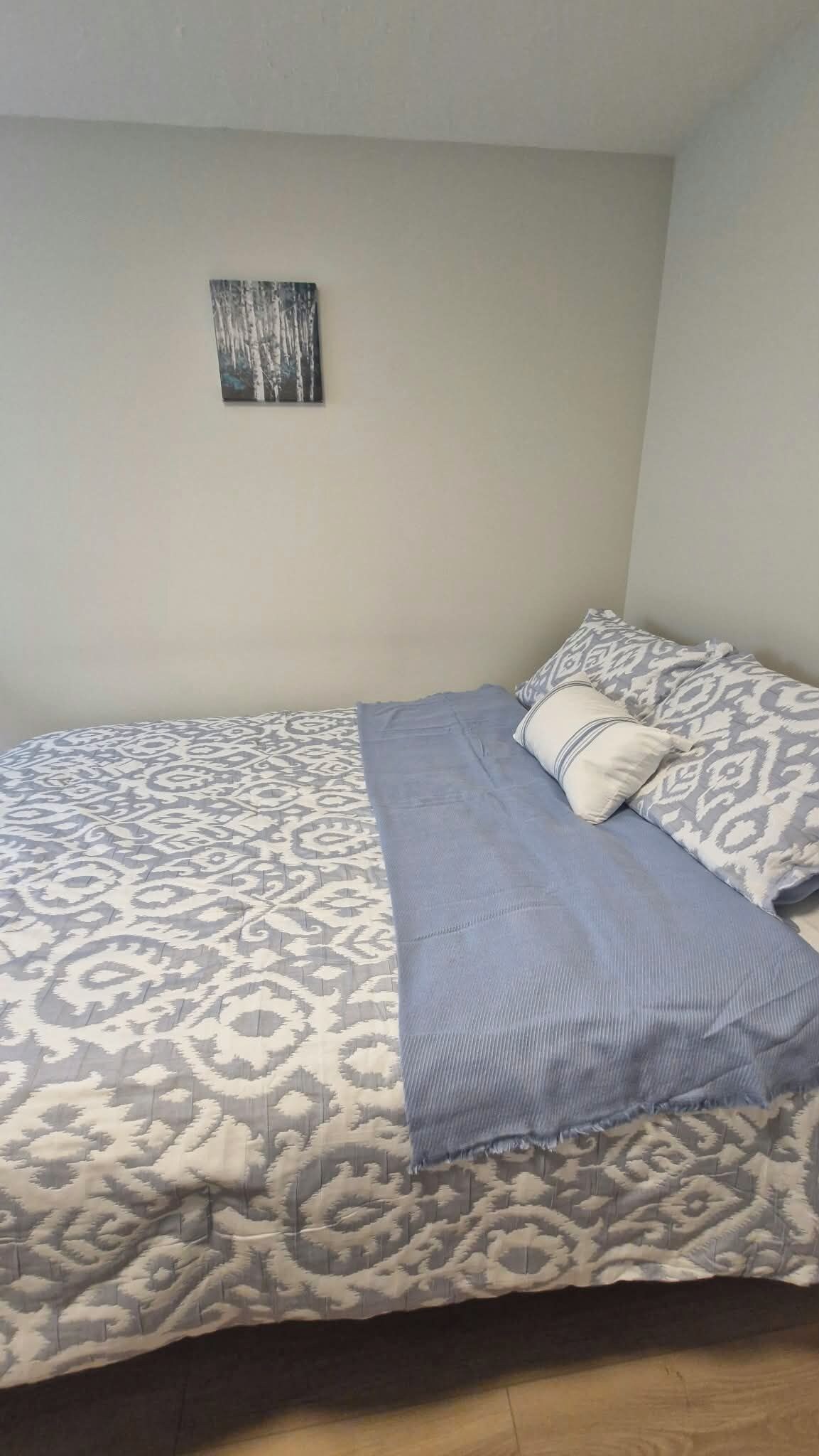 Une chambre à coucher avec une couvre-lit à motifs, un seul oreiller et un petit tableau encadré accroché au mur.