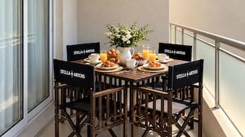 A balcony with a round table set for breakfast, featuring a vase of flowers, a pitcher, and various breakfast items.