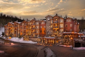 Un hotel de varios pisos con fachada de piedra, varios balcones y un paisaje cubierto de nieve.