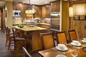 Una cocina moderna con armarios de madera, electrodomésticos de acero inoxidable y una zona de comedor con mesa para cuatro.