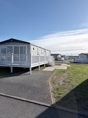 A caravan park with multiple caravans, a paved walkway, and a grassy area. - Ambleside Lodge Sleeps 6 with Parking and Wrap Around Balcony (Porthmadog)