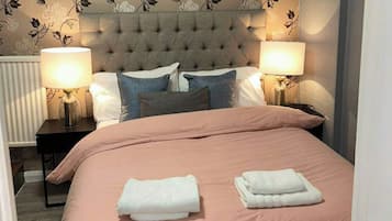 A neatly made bed with a pink bedspread, two white towels, and a tufted headboard.