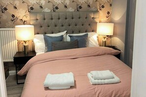 A neatly made bed with a pink bedspread, two white towels, and a tufted headboard. - Cosy 1 Bed Apartment Sleeps 3 with WiFi (Maidstone)