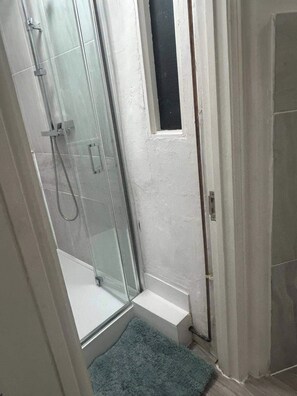 A shower area with glass doors, a small window, and a blue mat. - Cosy 1 Bed Apartment Sleeps 3 with WiFi (Maidstone)