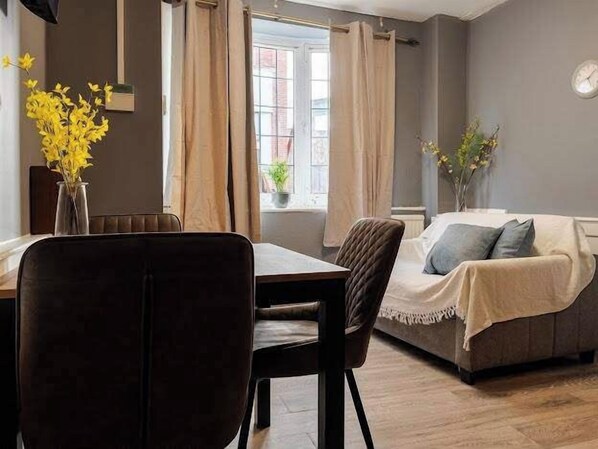 A room with a dining table, chairs, a sofa, and a window with curtains. - Cosy 1 Bed Apartment Sleeps 3 with WiFi (Maidstone)