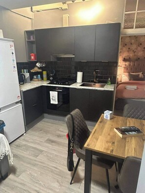 A compact kitchen with dark cabinetry, a gas stove, and a dining area with a table and chairs. - Cosy 1 Bed Apartment Sleeps 3 with WiFi (Maidstone)