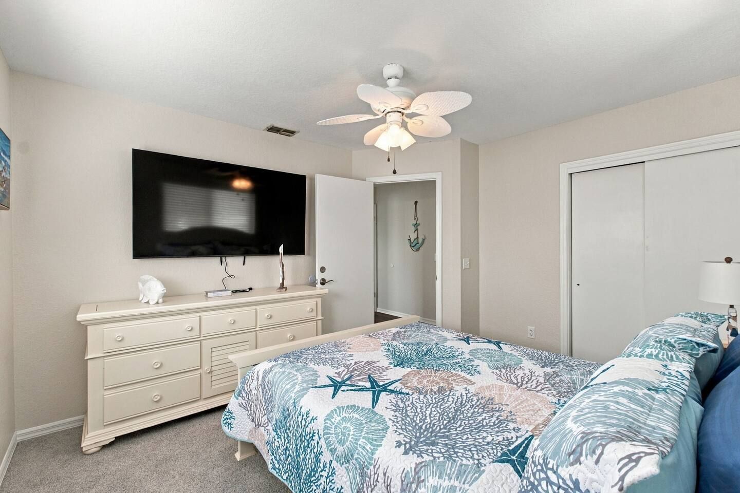 A bedroom with a bed, dresser, TV, ceiling fan, and a door.