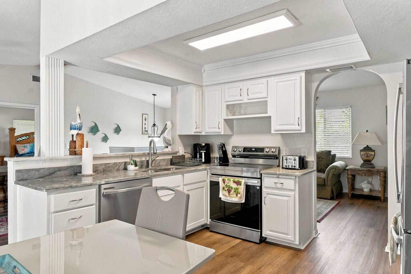 A modern kitchen with white cabinetry, a stainless steel stove, and a dining area with a white table.