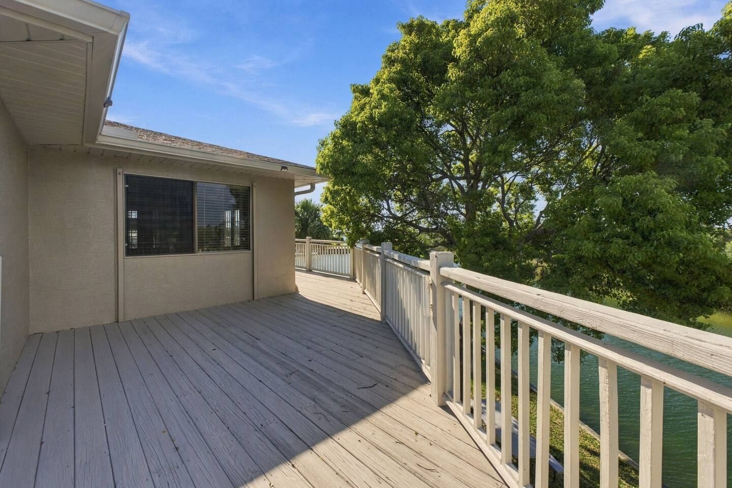 A wooden deck with a railing, a window, and a tree in the background.