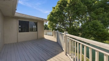 A wooden deck with a railing, a window, and a tree in the background.