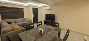 A living room with a sofa, dining table, chairs, a TV, and an air conditioning unit. - New Listing (Ensenada)