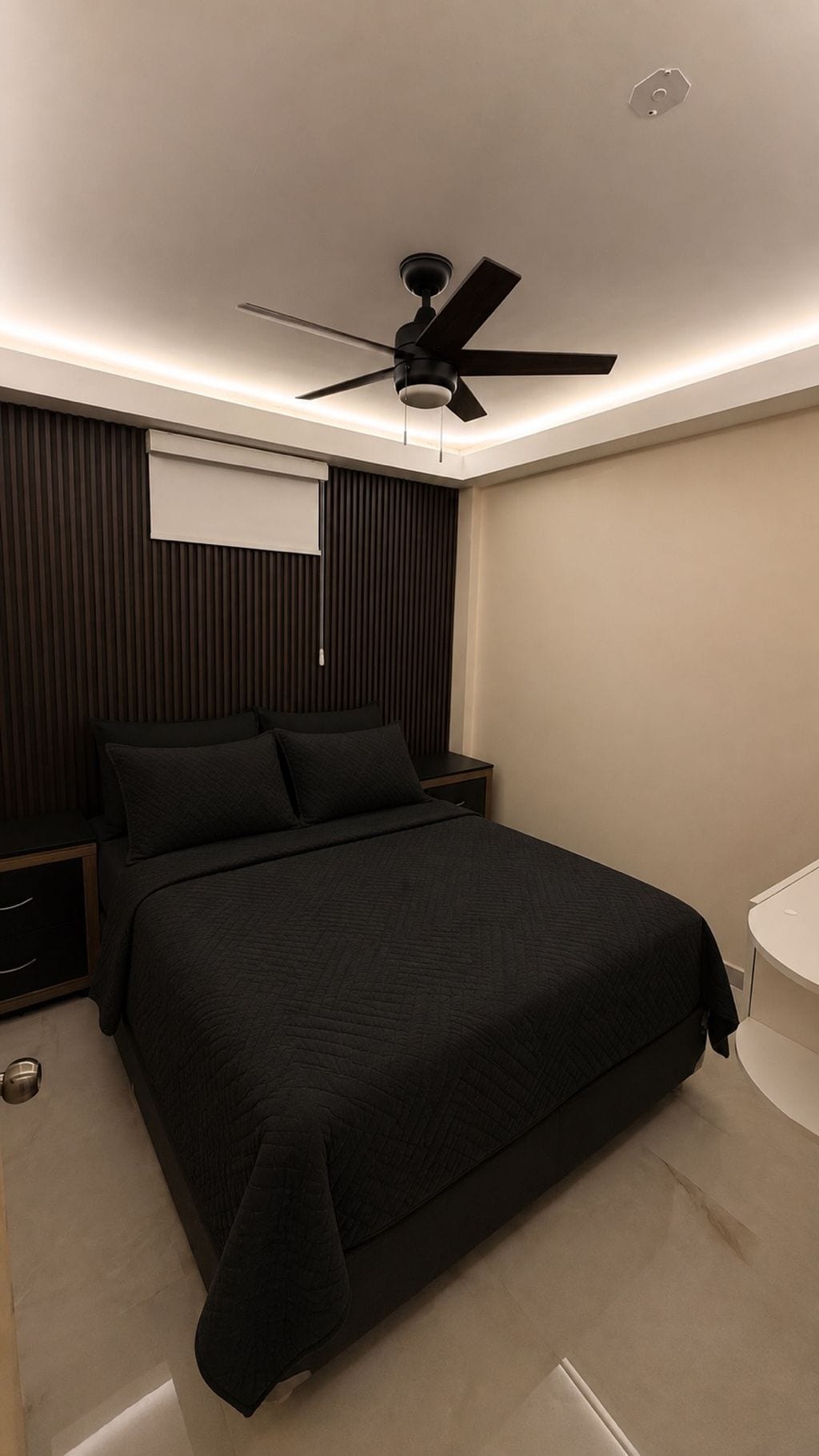 A modern bedroom with a bed, a ceiling fan, and a bedside table.