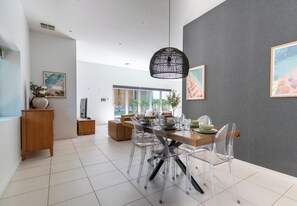 Uma área de refeições moderna com mesa de madeira, cadeiras transparentes e luminária pendente preta.