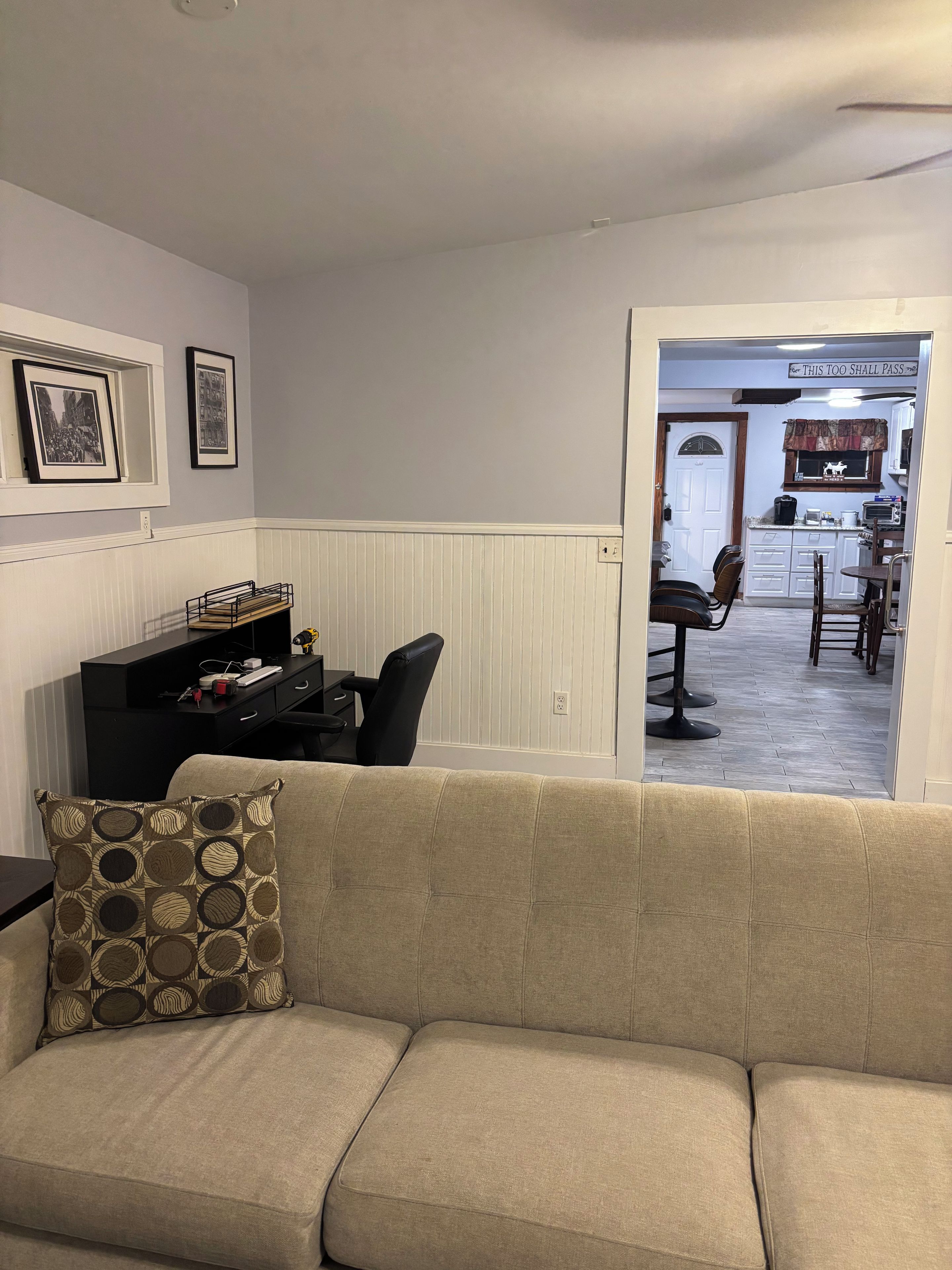 Un salon avec un canapé beige, un meuble de télévision noir et des tableaux encadrés accrochés au mur.