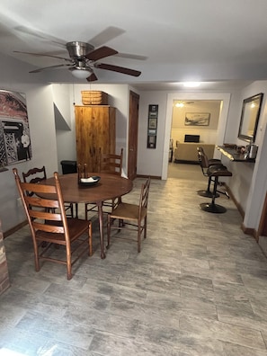 Un coin repas avec une table ronde, des chaises en bois, un ventilateur de plafond et un mur en briques.