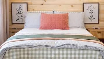 A bed with a checkered bedspread, two bedside lamps, and framed botanical prints on the wall.