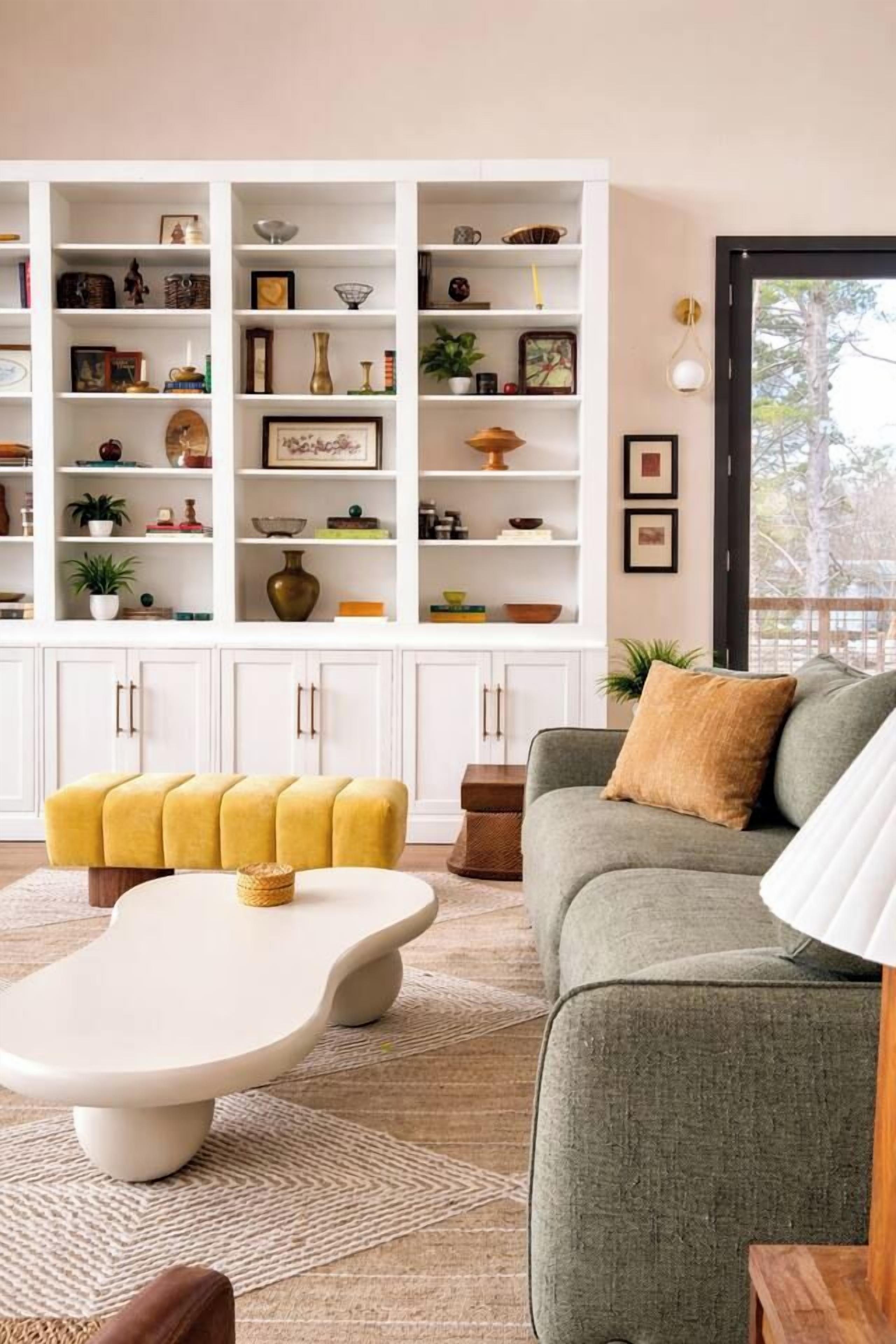 A living room with a sofa, a coffee table, and a bookshelf filled with various items.