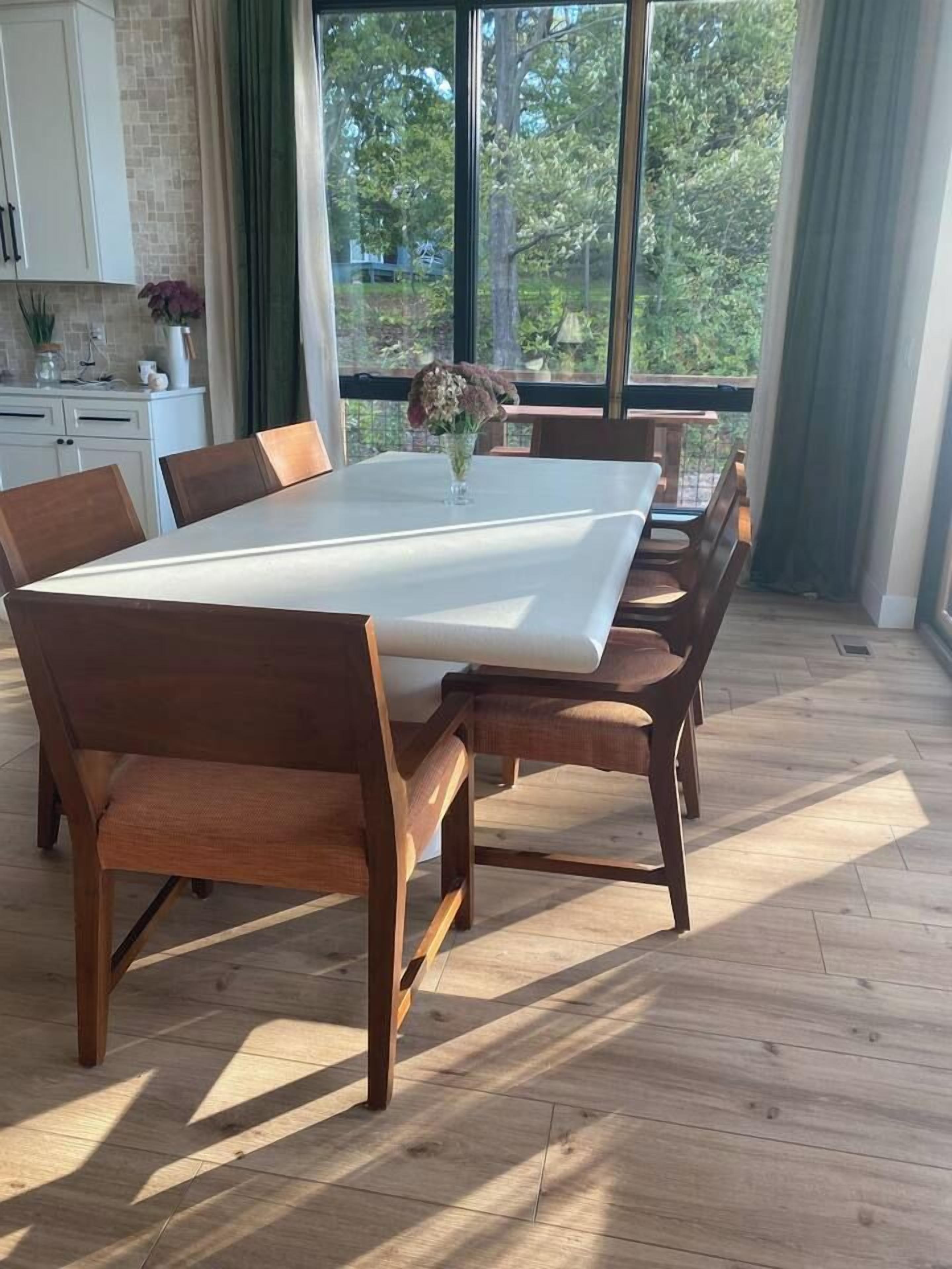 A dining area with a large rectangular table, wooden chairs, and a vase with flowers.