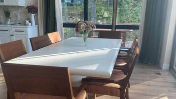 A dining area with a large rectangular table, wooden chairs, and a vase with flowers.