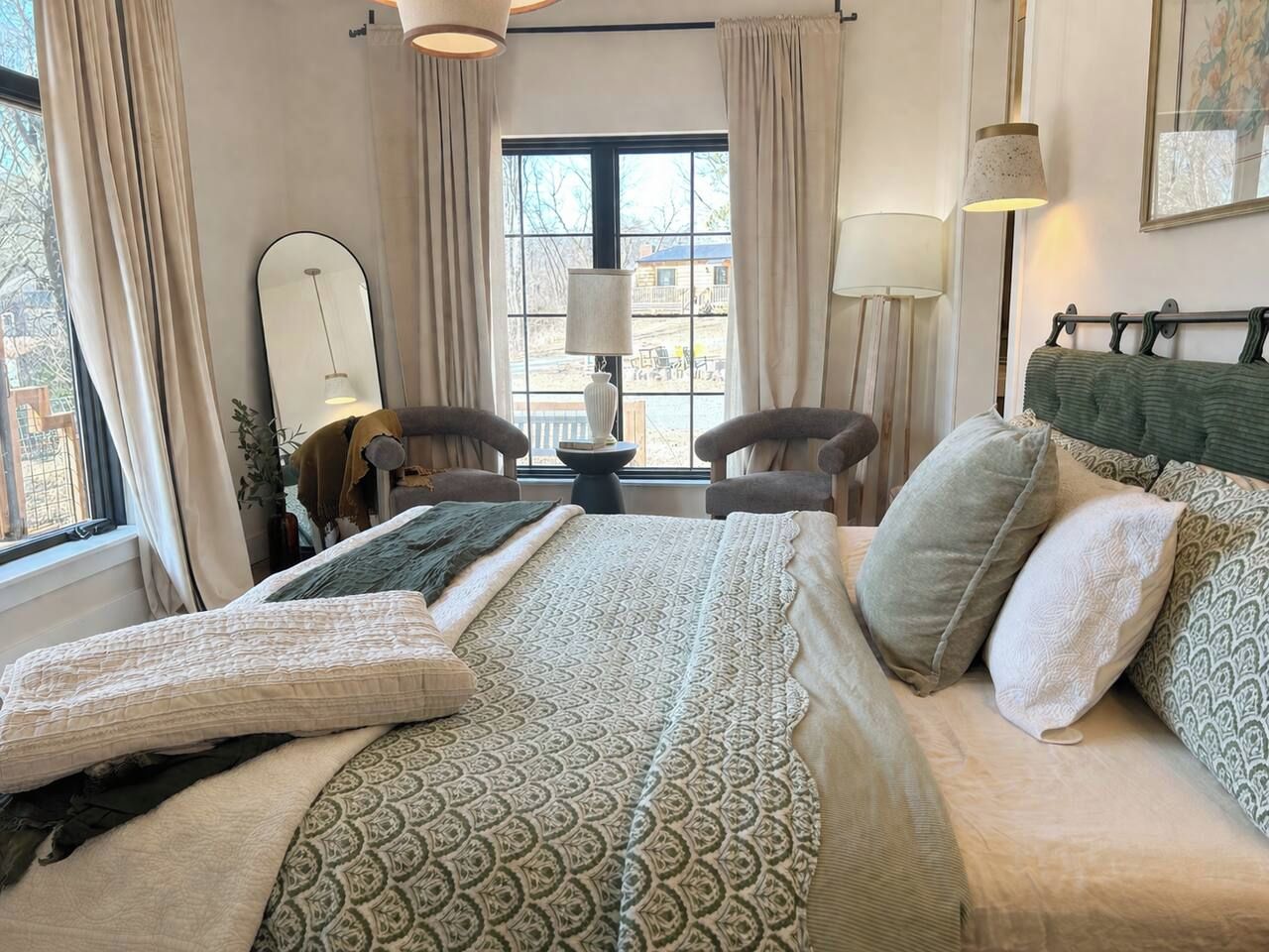 A hotel room with a large bed, two armchairs, a table, and a window with curtains.