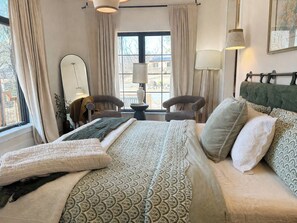 Ein Hotelzimmer mit einem großen Bett, zwei Sesseln, einem Tisch und einem Fenster mit Vorhängen.