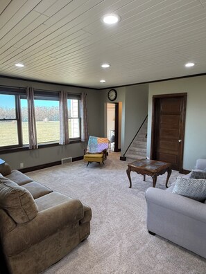 A living room with a sofa, ottoman, coffee table, and a view of the outdoors. - Peaceful Plains Farmhouse - 3BR retreat near Medora (Beach)
