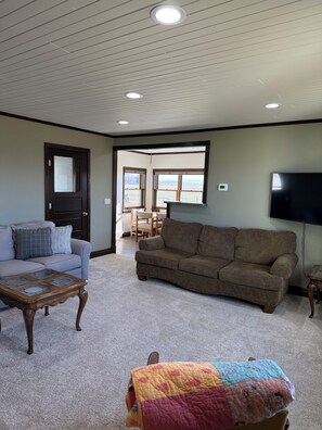A living room with a sectional sofa, a coffee table, and a TV mounted on the wall. - Peaceful Plains Farmhouse - 3BR retreat near Medora (Beach)
