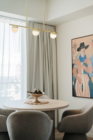 A dining area with a round table, four chairs, a bowl of fruit, and a painting on the wall. - Salt and Soleil a beachside apartment in the heart of the Gold Coast (Surfers Paradise)