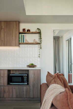 A modern kitchen with a built-in microwave, wooden cabinets, and a shelf with books and decorative items. - Salt and Soleil a beachside apartment in the heart of the Gold Coast (Surfers Paradise)