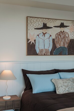 A bedroom with a bed, pillows, a nightstand, a lamp, and a wall-mounted painting. - Salt and Soleil a beachside apartment in the heart of the Gold Coast (Surfers Paradise)