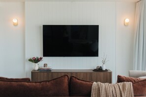 A modern living room with a flat-screen TV mounted on a white paneled wall, a wooden console table with books and decorative items, and brown upholstered sofas. - Salt and Soleil a beachside apartment in the heart of the Gold Coast (Surfers Paradise)