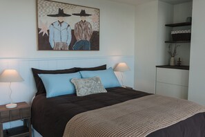 A bedroom with a bed, two bedside lamps, a nightstand, a dresser, and a wall-mounted artwork. - Salt and Soleil a beachside apartment in the heart of the Gold Coast (Surfers Paradise)