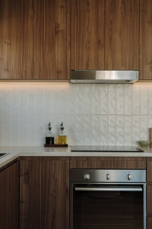 A kitchen with wooden cabinets, a stainless steel range hood, a white tiled backsplash, and a built-in oven. - Salt and Soleil a beachside apartment in the heart of the Gold Coast (Surfers Paradise)