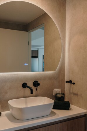 A bathroom with a white vessel sink, a mirror with an arched top, and a towel rack. - Salt and Soleil a beachside apartment in the heart of the Gold Coast (Surfers Paradise)