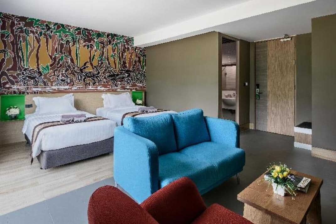 Ein Hotelzimmer mit zwei Betten, einem blauen Sofa, einem Holztisch und einem farbenfrohen, abstrakten Wandgemälde.