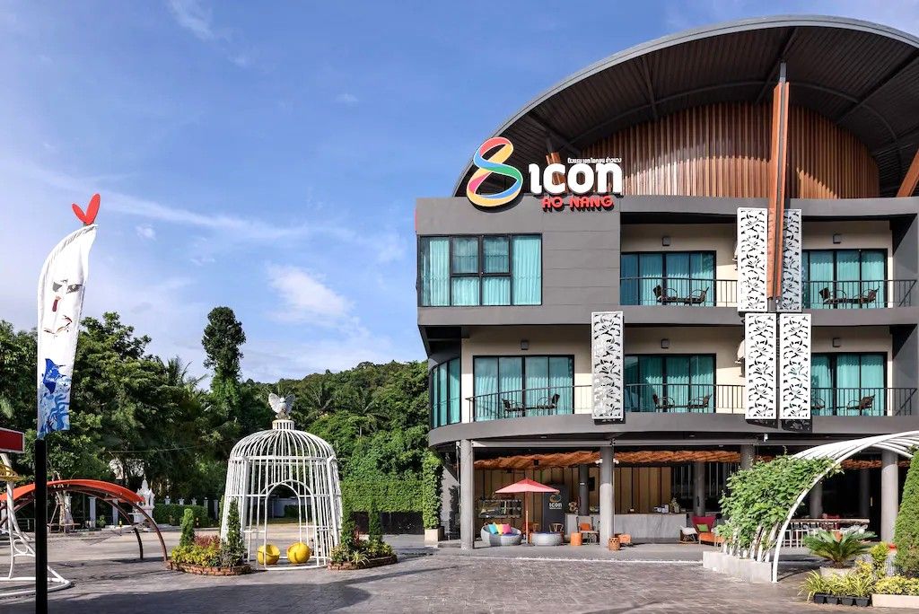 A multi-story hotel with a modern design, featuring balconies, large windows, and a central atrium with seating areas.
