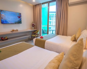 A hotel room with two beds, a TV mounted on the wall, a small table with a vase of flowers, and a view of the outside through a large window. - Galilea Hotel Bohol (Tagbilaran)