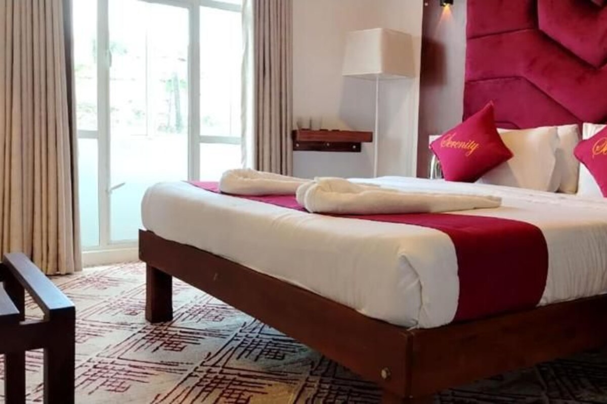 Quarto de hotel com uma cama grande, cabeceira de madeira e vista pela janela.